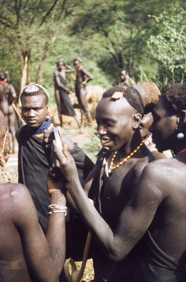 Henry's shaving mirror'. A Suk (Pokot) porter, working with a British forestry survey team, smiles with delight on seeing his reflection in the shaving mirror of Henry Osmaston (Working Plans Officer, Uganda Forest Department) on a safari to the Karasuk hills. Kenya, May 1959., East (Uganda), Uganda, Eastern Africa, Africa.