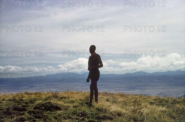 Porter on the summit of Mount Napak. A porter working with a British forestry survey team stands silhouetted against the skyline on the summit of Mount Napak, overlooking Karasuk on the Kenya-Uganda border. North East Uganda, December 1958., East (Uganda), Uganda, Eastern Africa, Africa.