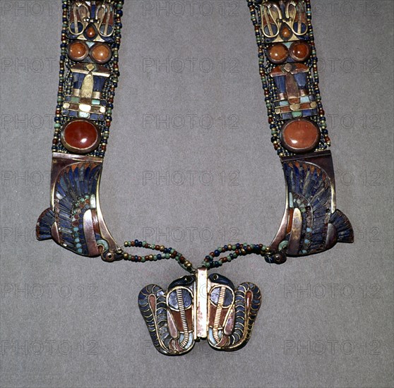 The counterpoise of a scarab pectoral from the tomb of Tutankhamun with straps formed from inlaid plaques with uraei (cobras), scarabs & solar discs