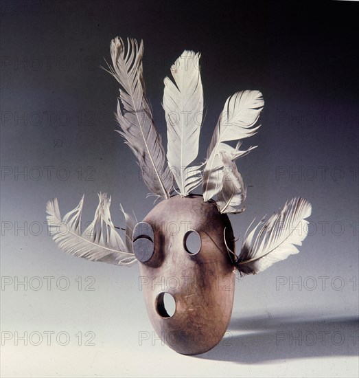 A mask of wood and feathers which bears a black eye, perhaps a humorous detail to the shaman who carved it