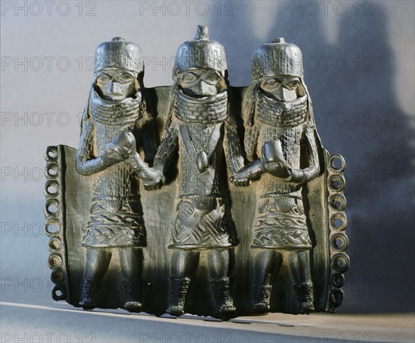 A chief with attendants depicted on a damaged brass pectoral ornament part of the ceremonial regalia of a Benin chief