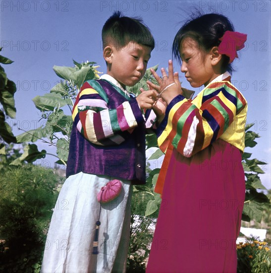 Two young Korean children in traditional dress playing Cat's Cradle