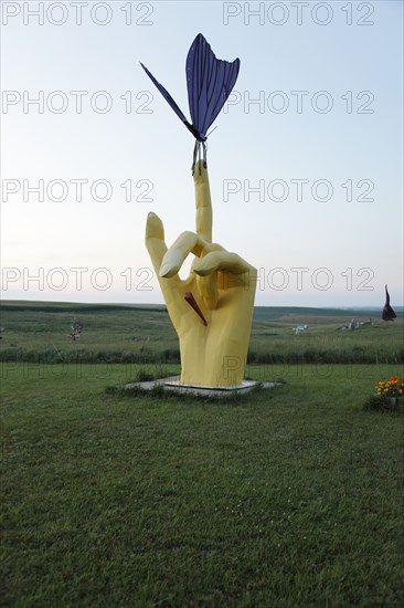 Hand with finger extended holds a butterfly; Located just off Interstate 90 in the South Dakota Drift Prairie, about 25 miles west of Sioux Falls. Many of the sculptures, in the style of industrial art, were made with scrap metal, old farm equipment, or railroad tie plates. 2006