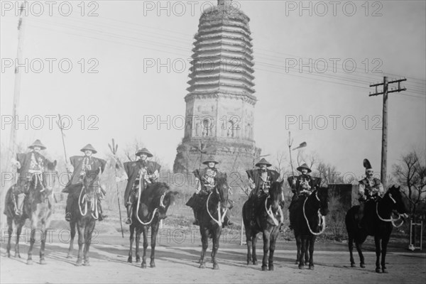 7 Chinese Gendarmes in peaked hats are mounted as skirmishes as cavalry in front of a temple.