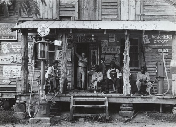 African American and a white store owner on the Porch of a country store 1939