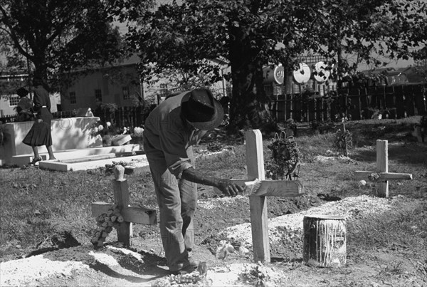 African American paints the crucifix marking a gravesite in a cemetery 1938