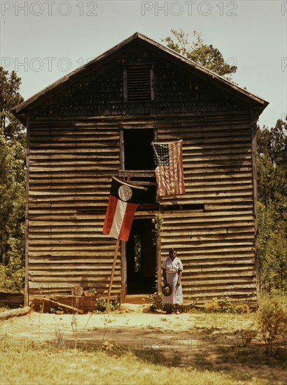 African American woman standing by building with Georgia state and United States flags. 1941
