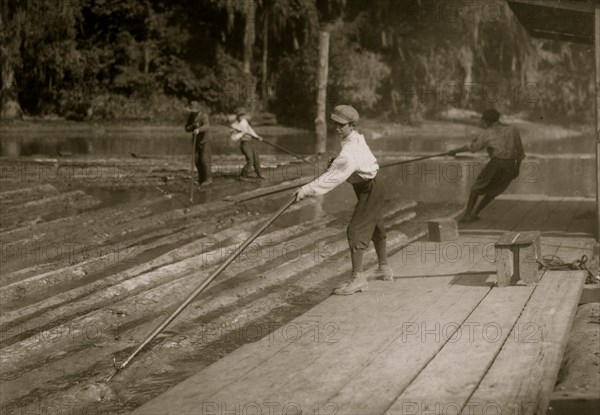 Hard work and dangerous. This "river-boy" Lyman Frugia. Poles the heavy logs into the incline that takes them up to the mill.  1914