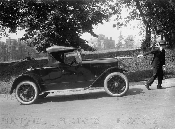 Suited man looks like he is pulling a coupe up an incline by a string