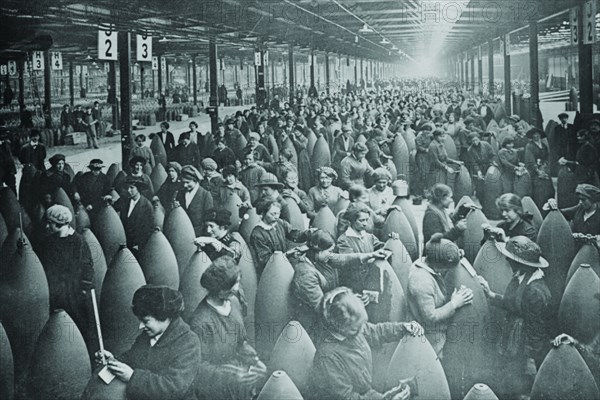 Throngs of women interspersed amongst large artillery shells on a factory floor. 1917