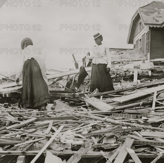 Two African American women search through rubble following a violent hurricane which devastated most of Galveston and took more than 5,000 lives. 1900