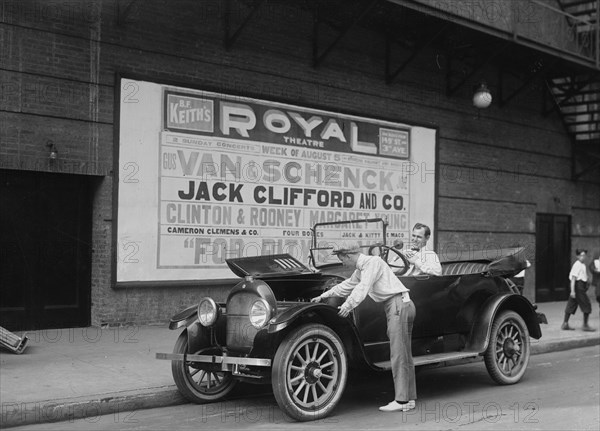 Two performers work on their car, one in the driver' seat and the other looks under the hood; Van & Schenk