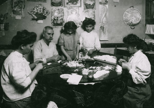 Whole family rolling cigarette cases, the mother was licking the papers as she worked. 1924