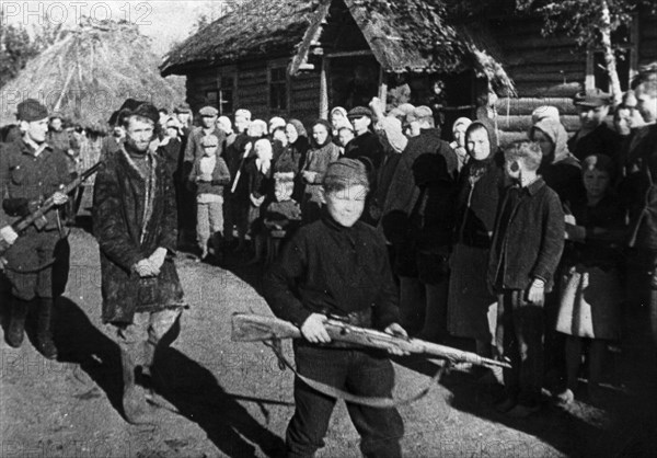 World war 2, a russian traitor being marched from the open air courtroom where he had been judged by the villagers, the procession is being led by a 13 year old guard, a full-fledged partisan scout, from an artkino film, 'people's avengers'.