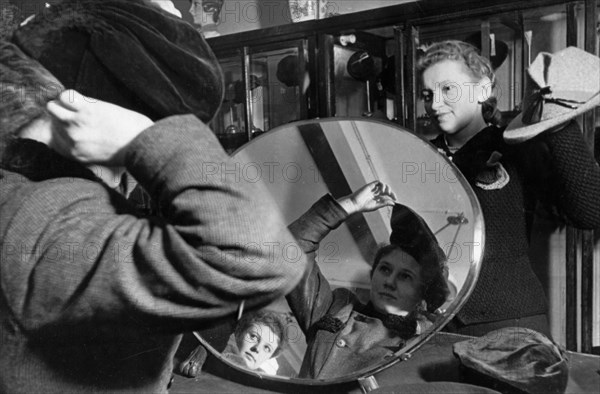 A young woman trying on a hat in the central department store of moscow, late 1930s.