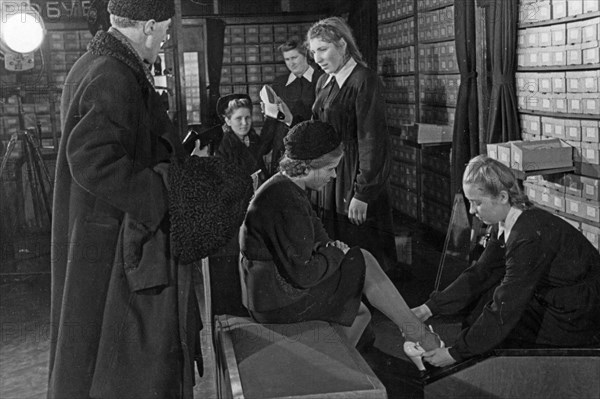 A woman trying on shoes in the footware department of a moscow department store, december 1947.