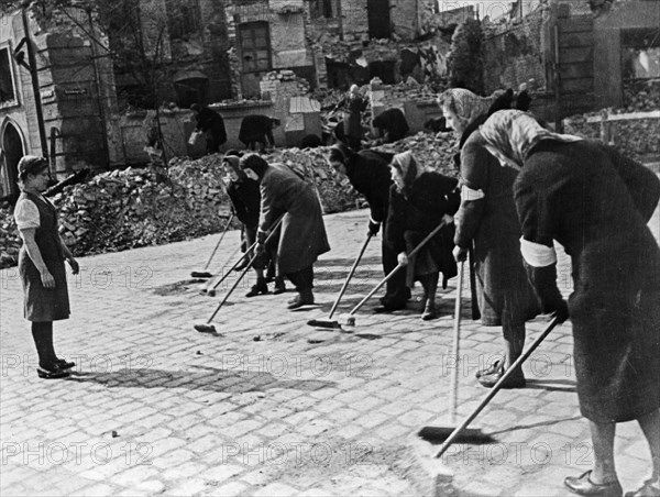 German women sweeping a berlin (?) street after the german surrender at the end of world war 2 in 1945, they are being supervised by marusia kuznetsova, a russian girl who spend more than 2 years as a slave laborer.