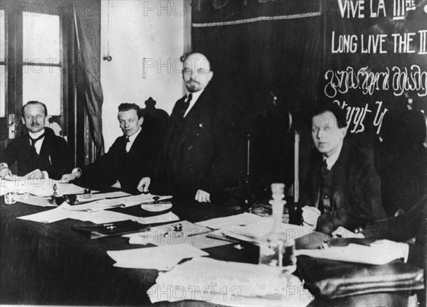 V,i, lenin (standing) presides at first congress of comintern (third international) in kremlin, march 1919, moscow, soviet union, left to right: klinger, eberlaine (?), lenin, f, patten (?), legend on blackboard (in several languages): 'long live the third international'.