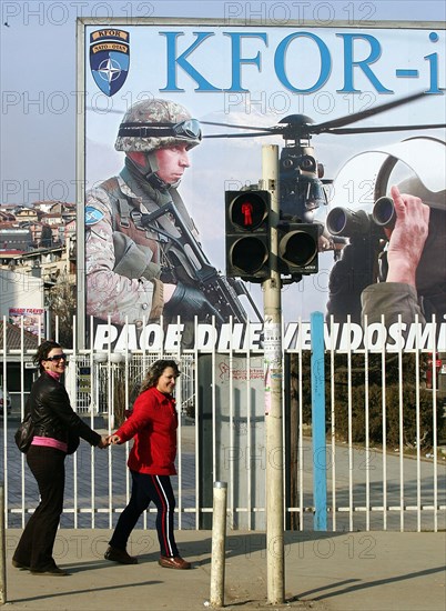 Young kosovan women at the traffic lights in pristina, with a billboard ad promoting kfor and nato in the background, kosovo, february 25, 2008.