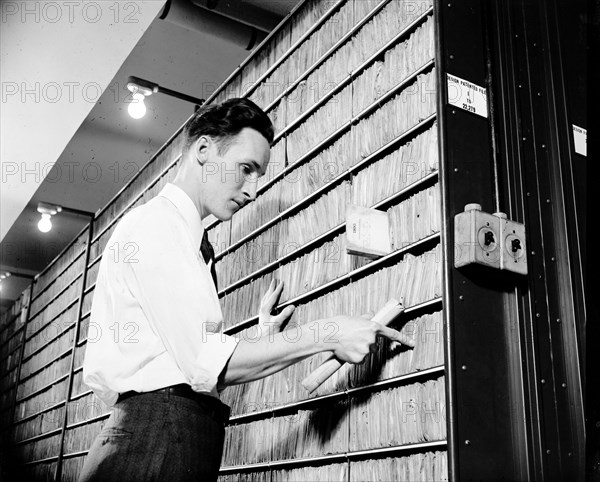 Patent Office employee pointing to copies of first patent granted after 1836 when patent laws were rewritten circa 1940.