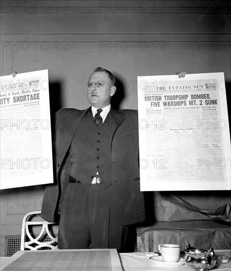 Man holding up The Evening Sun newspaper headlines about Germans sinking British ships circa 1940 .