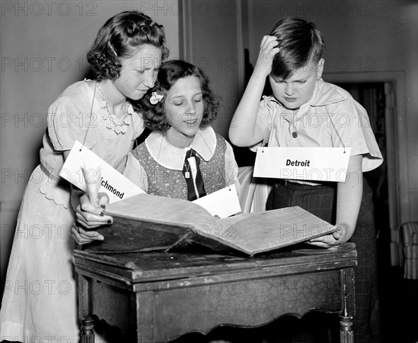 The Courier-Journal spelling bee participants in staged photo, looking up words in a dictionary, 1940.