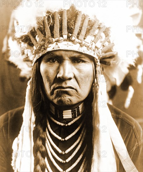 Edward S. Curtis Native American Indians - Nez Percé man in full feather headdress, braided hair, and necklaces circa 1910.