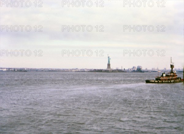 (R) New York 1975 - Tugboat in water in front of Statue of Liberty in New York City in mid-1970s.