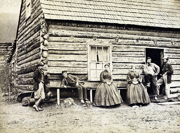 Frontier family outside their log cabin