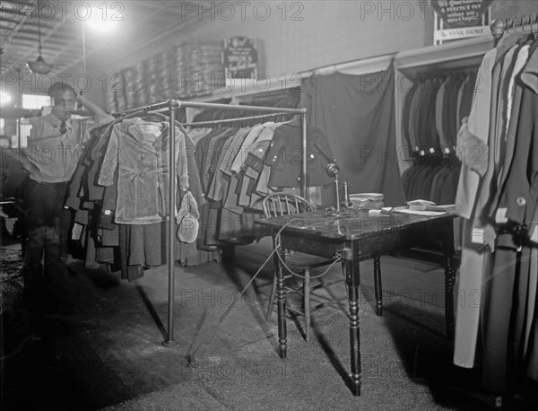 Worker standing next to a rack of cloethes in a clothing store ca. between 1910 and 1935