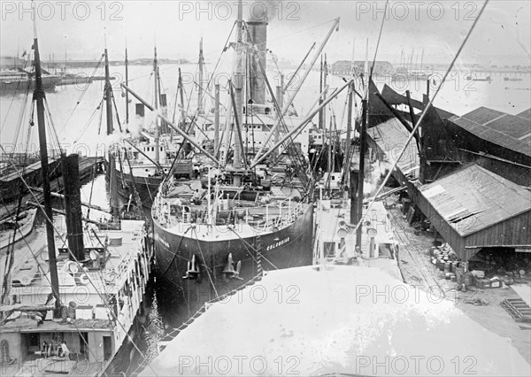 Steamer loading sugar alongside dock in Honolulu, [Hawaiian Islands]. The small steamers are discharging sugar into large one. ca.  between 1910 and 1920