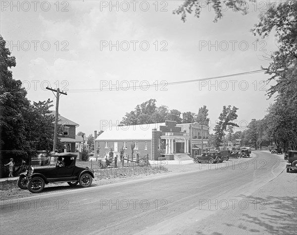 Early 1900s street scene, car driving down a road in small town ca.  between 1918 and 1928