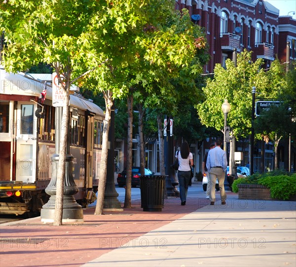 A man and woman walking north on McKinney Avenue in the Uptown area of Dallas, TX; a trolley car stopped on the street