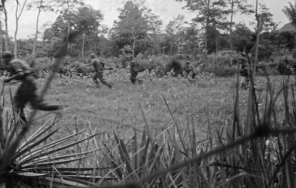 Dutch soldiers run across an open field with weapons at the ready in Indonesia, Dutch East Indies, Sumatra ca. December 25, 1948