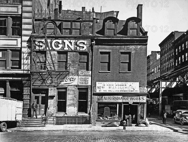 1930s New York City - Sign company with decorative ironwork along roof, auto radiator shop, in three-story buildings, the elevated railroad just visible at right. Broome Street, Nos. 504-506, Manhattanca. 1935