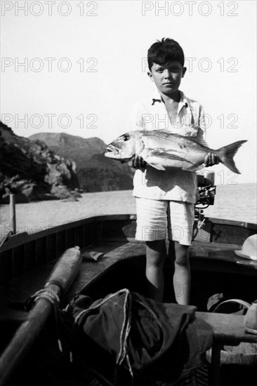 Italy. Tuscany. Capraia Island. Portrait Of A Baby With Dentex. 1930-40