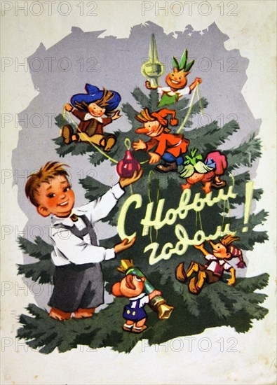 A little boy holds a Christmas tree toy in his hands against the background of a Christmas tree decorated with figurines of fairy tale characters.