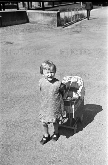 Boy playing with baby carriage for doll, 1938