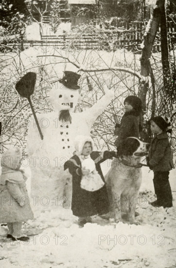 In this early 1900s photo, children and a dog stand by a newly made snowman.