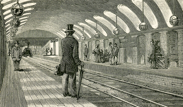 This illustration dates to the 1870s and shows the Gower Street Train Station in England in the 1870s - a stop for the Metropolitan railway. The booking offices for the up line are on one side of the road, and those for the down line on the other. This view represents the interior of the Gower Street Station. In each the platforms are 325 ft. long and 10 ft. broad, and the stations are lighted by lateral openings through the springing of the arch which forms the roof. This arch is a portion of a circle of 32 ft. radius, with a span of 45 ft. and a rise of 9 ft. at the crown. The lateral openings are arched at the top and bottom, but the sides are flat. The width of each is 4 ft. 9 in., and the height outside 6 ft., increasing to 10 ft. at the ends opening on the platform. The openings are entirely lined with white glazed tiles, and the outward ends open into an area, the back of which is inclined at an angle of 45¬8, and the whole also lined with white glazed tiles, and covered with gl...