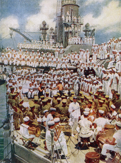 The caption reads: ""Pack up your troubles in your old sea bag. All work and no play was not permitted to make the American sailor a dull boy."" The image dates to 1922 and shows American military on a carrier at sea in World War I. In the foreground a band with a conductor. In the middle is a boxing matched watched by a number of sailors. The others are more sailors and crew watching the events.