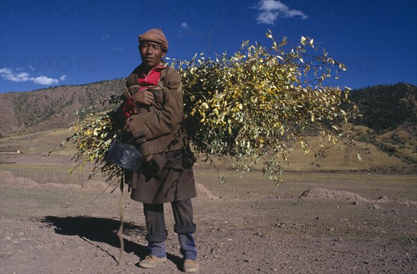CHINA, Tibet, Markam, Man carrying roofing materials on his back