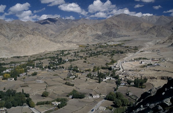 INDIA, Ladakh Region, View over valley with scattered houses and cultivated land surrounded by barren mountain landscape.