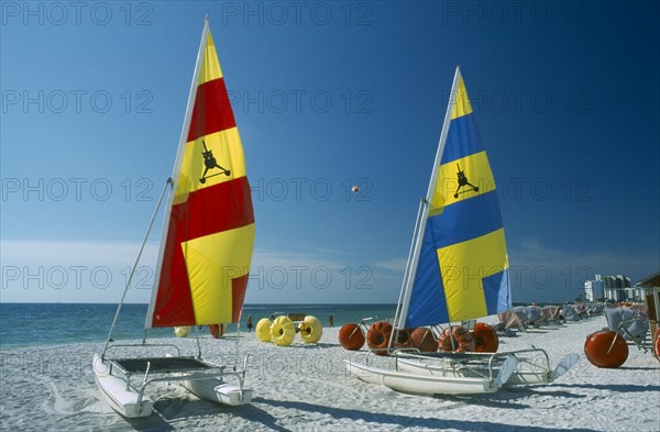 USA, Florida  , St.Petersburg, "Hobbie Cats with bright blue, red and yellow sails pulled up onto sandy beach."