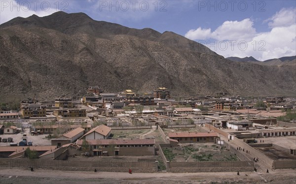 CHINA, Gansu, Xiahe, View over Labrang Monastery surrounded by hills and people walking a path in the foreground