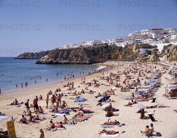 PORTUGAL, Algarve, Albufeira, View along the beach from above with sunbathers and the houselined headland beyond