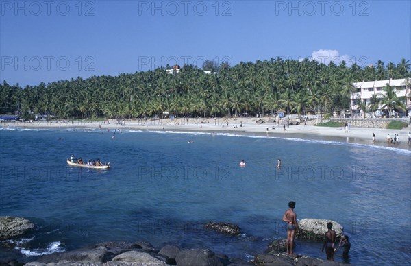 INDIA, Kerala , Kovalam Beach, View of beach with people swimming and a canoe.