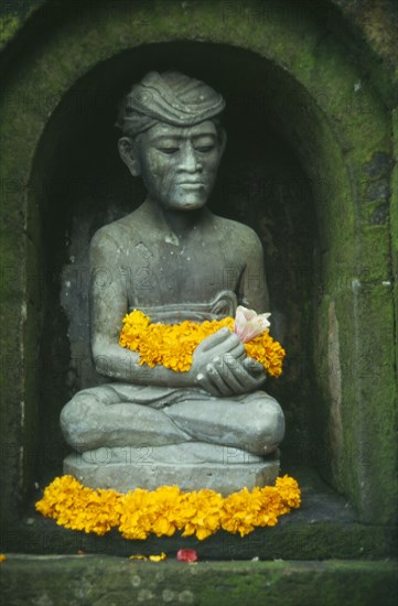 INDONESIA, Bali, Ubud, Small Hindu shrine detail of seated figure with flower offerings in the Miro Garden restaurant