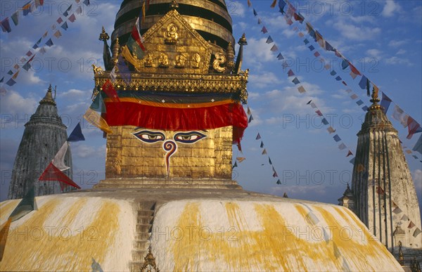 NEPAL, Kathmandu Valley, Swayambhunath, Swayambhunath Temple.  Detail of roof dome with painted face hung with prayer flags.
