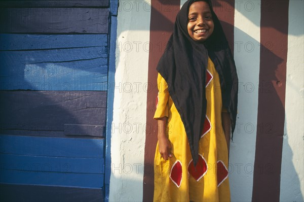 INDIA, Kerala , Kochin, Muslim girl standing in front of building wall painted with red and white stripes.